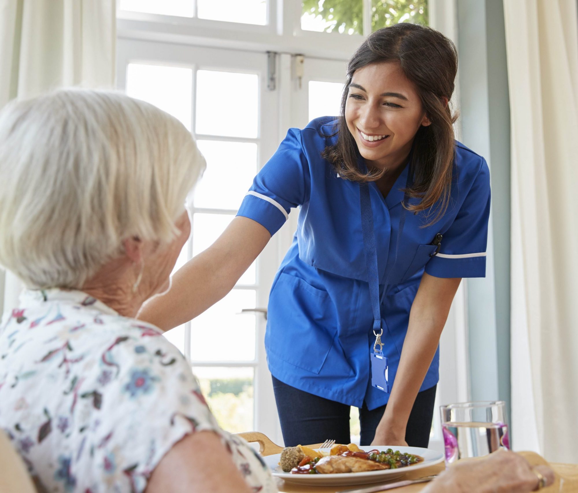 Care nurse serving dinner to a senior woman at home